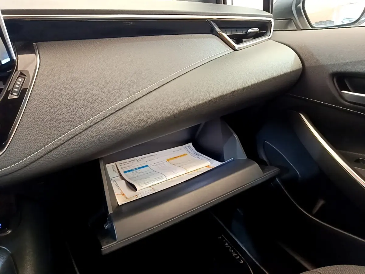 Intérieur côté passager de la Toyota Corolla hybride 2022, boîte à gants ouverte avec documents visibles, tableau de bord noir.