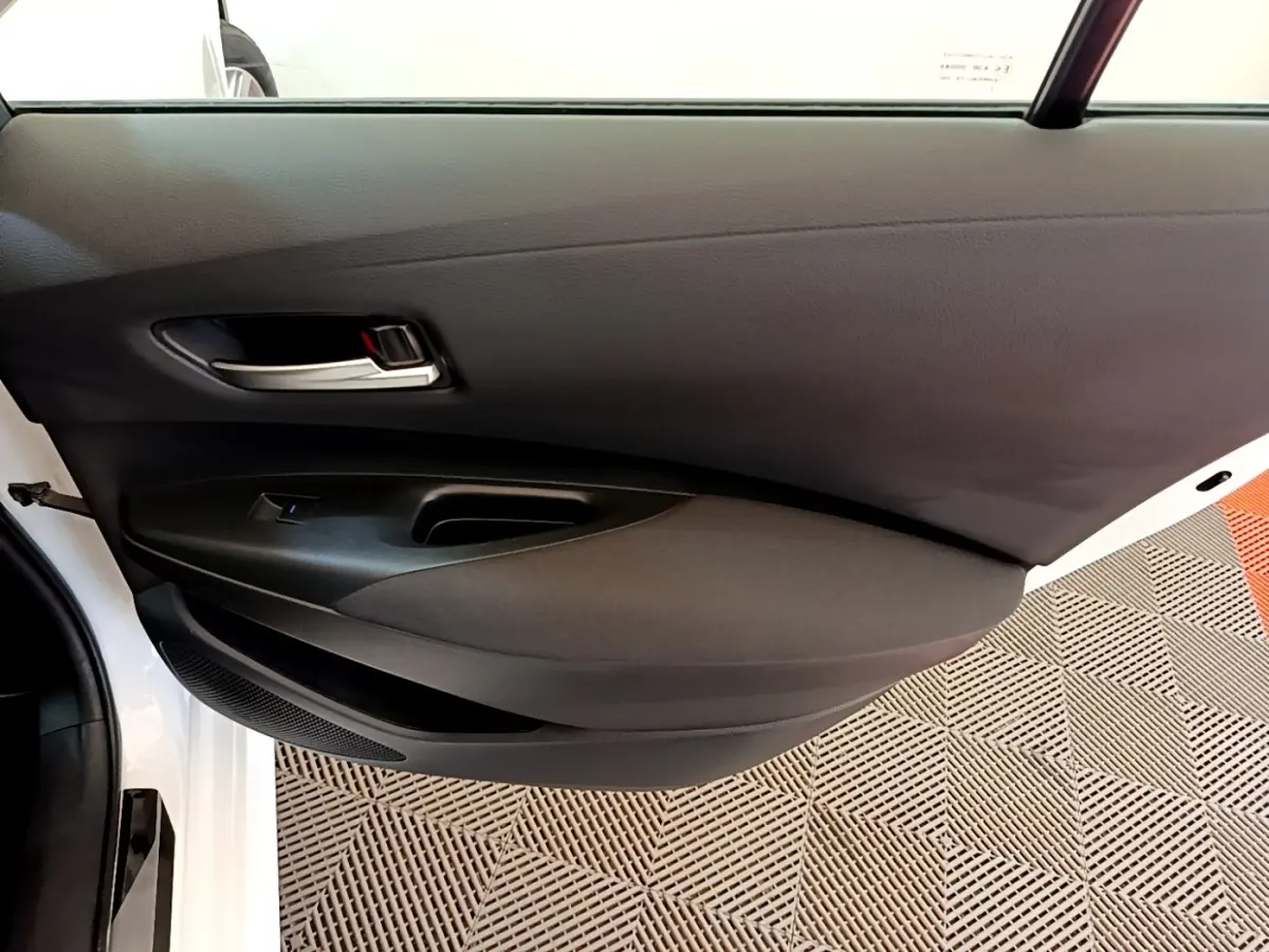 Vue rapprochée de la porte avant gauche noire de la Toyota Corolla hybride blanche, avec poignée argentée et bouton de vitre électrique.