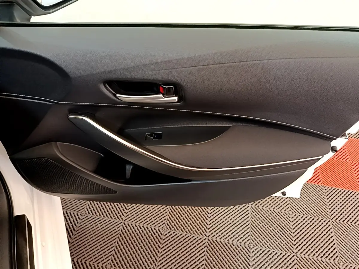 Vue intérieure côté gauche de la porte avant blanche d’une Toyota Corolla hybride avec poignée et garniture noire.