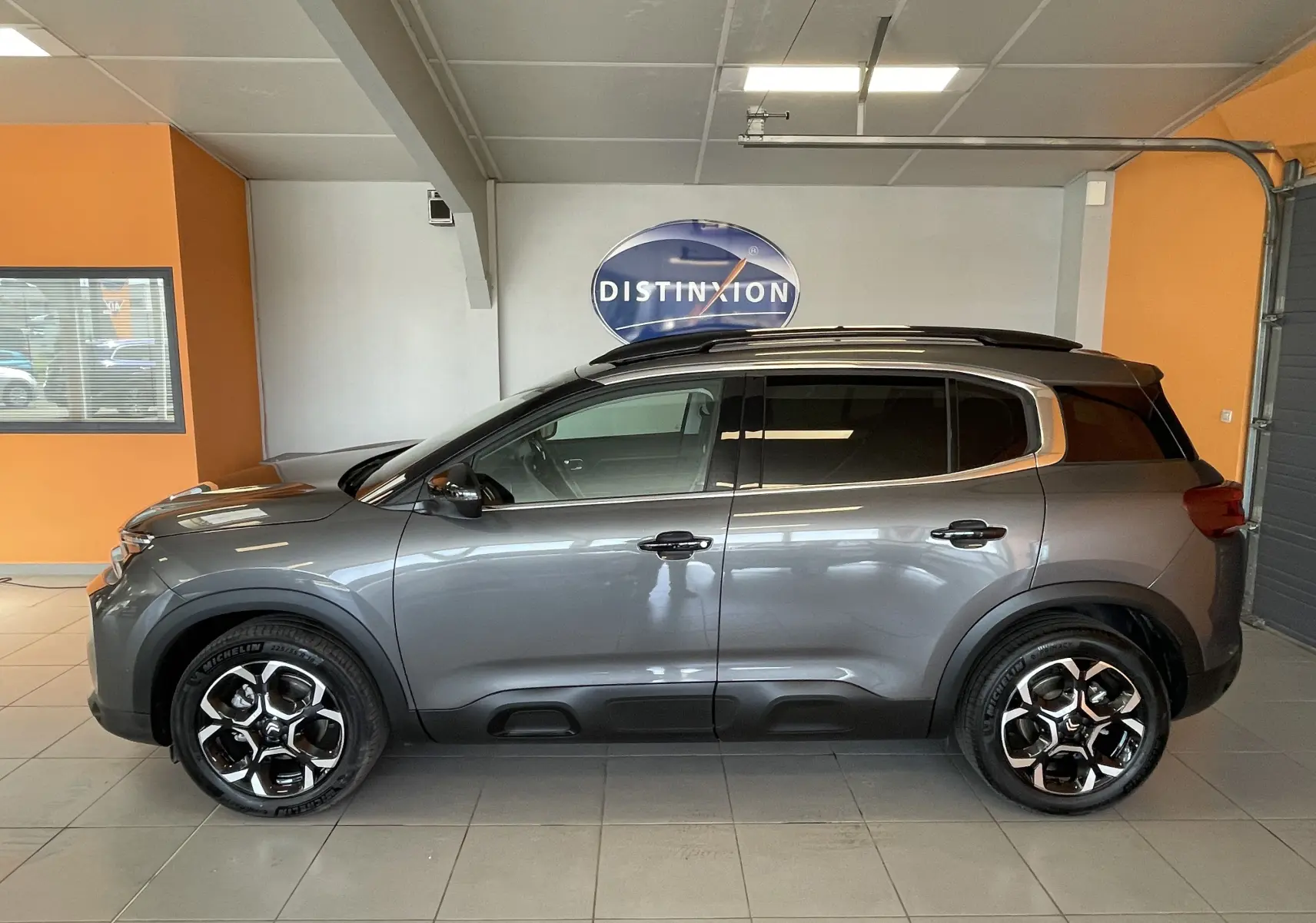 Vue latérale droite d'un Citroën C5 Aircross hybride gris platinium avec jantes alliage 18 pouces biton en intérieur showroom.