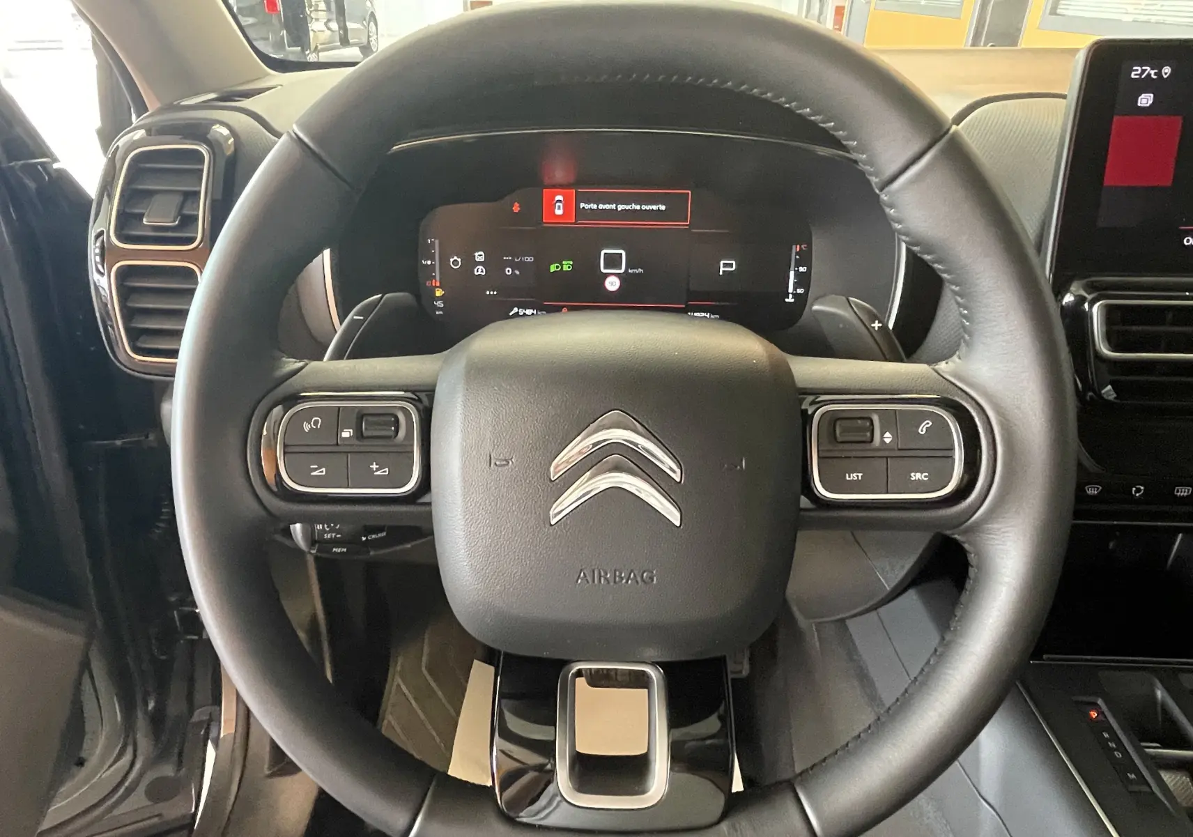 Vue rapprochée du volant en croûte de cuir noir du Citroën C5 Aircross hybride 2025, avec tableau de bord digital visible.