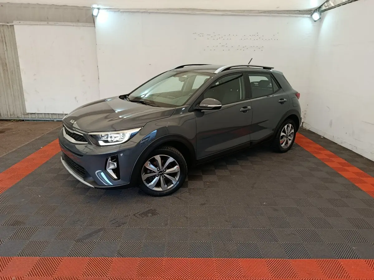 KIA Stonic gris foncé vue 3/4 avant droit dans un garage avec sol à damier noir et rouge.