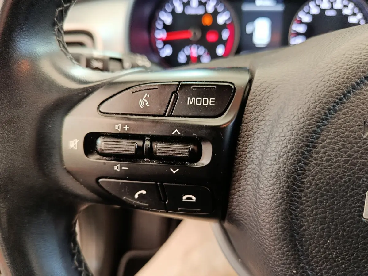 Gros plan sur les commandes du volant cuir noir de la Kia Stonic 2023, avec tableau de bord flou en arrière-plan.