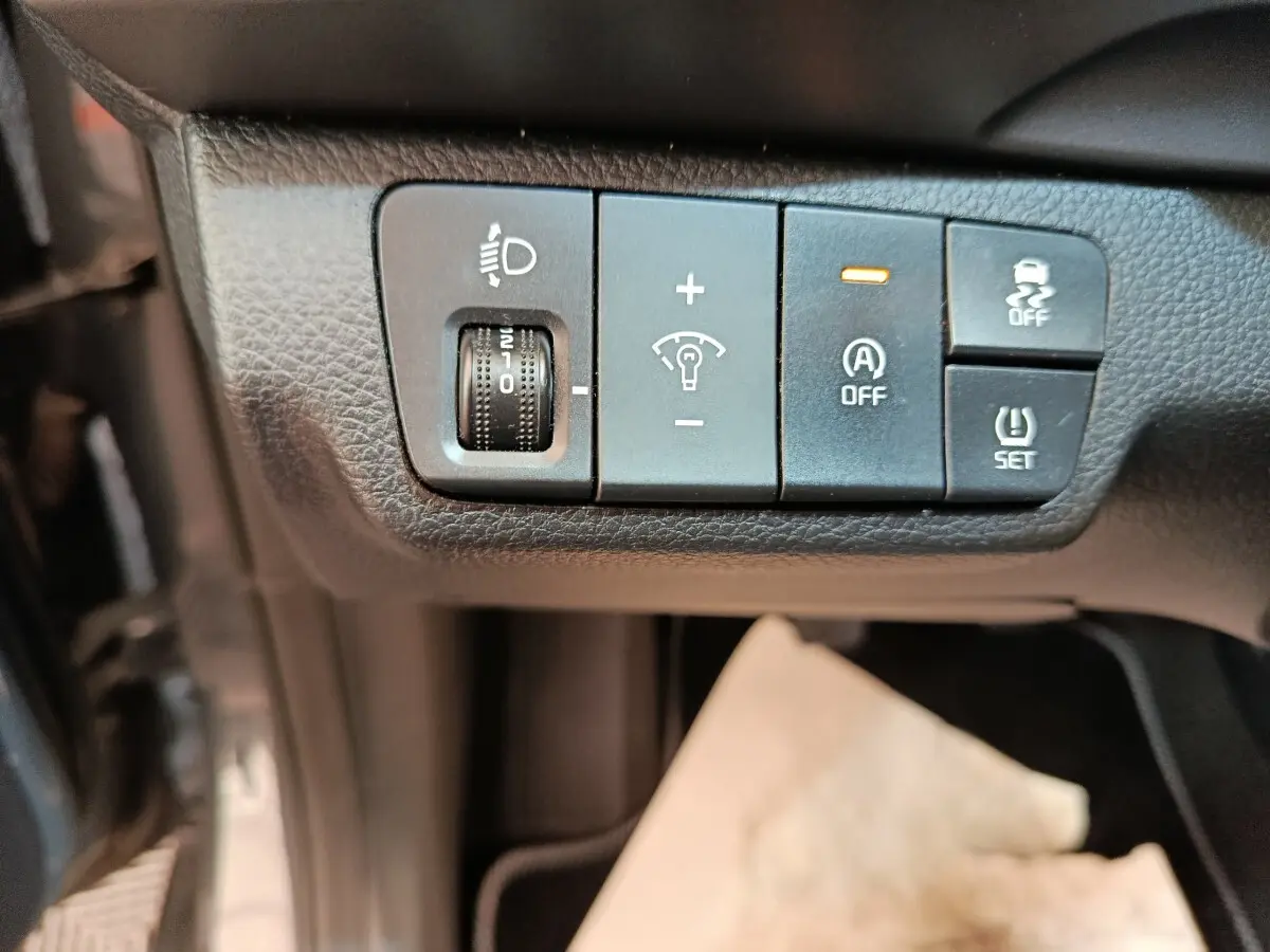 Gros plan sur les commandes de réglage des phares et aides à la conduite dans une Kia Stonic gris foncé, intérieur noir.