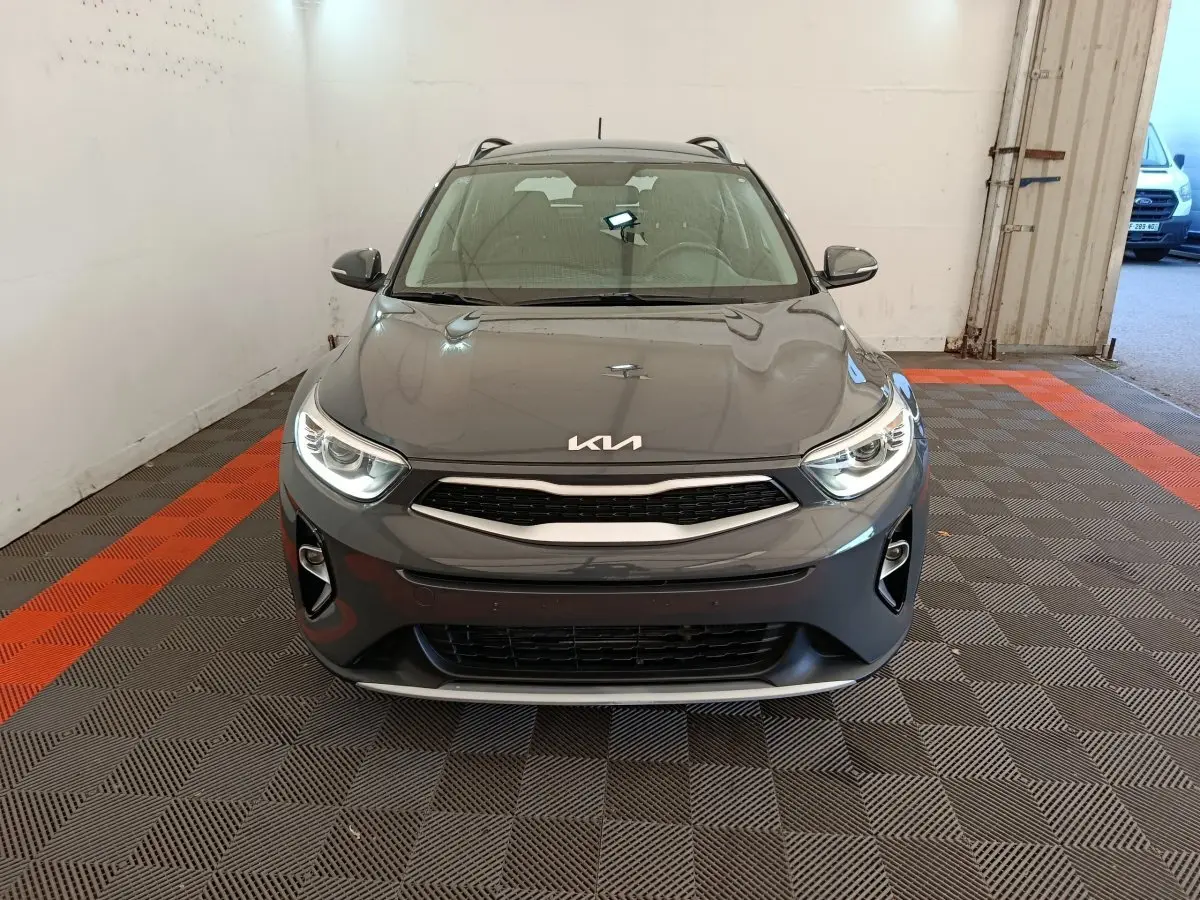 Vue frontale d'un KIA Stonic gris foncé 2023 avec phares allumés et calandre noire dans un garage.