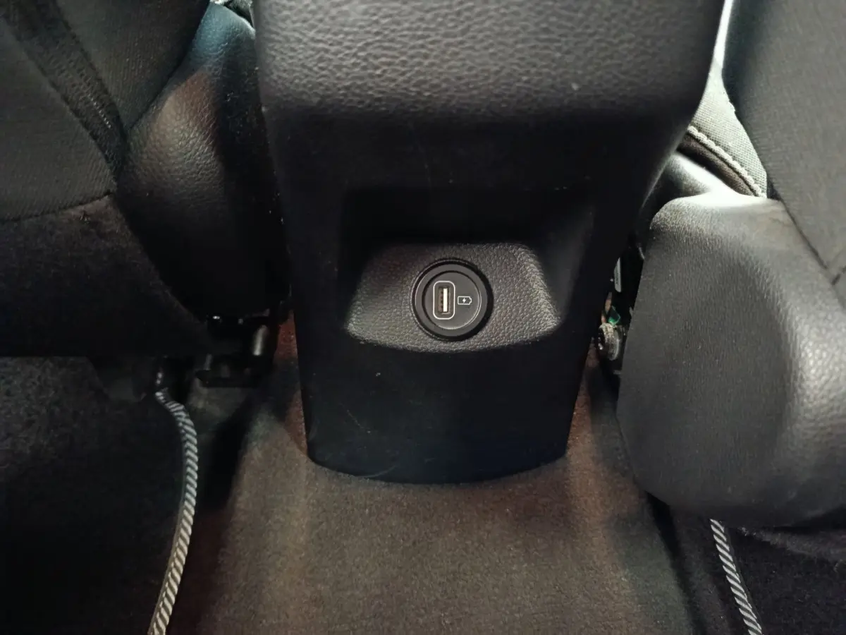 Prise USB arrière noire entre les sièges avant d’un Kia Stonic gris foncé, vue rapprochée du plancher.