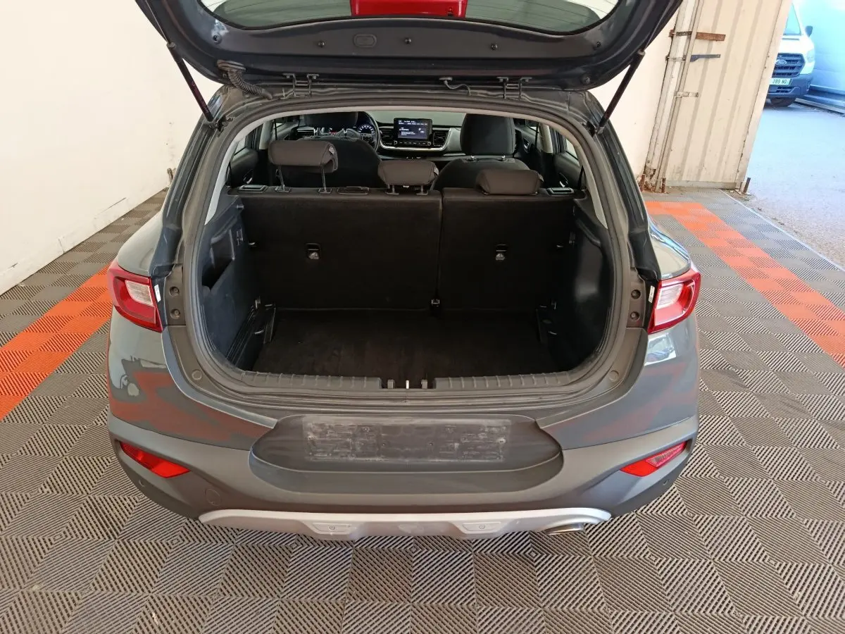 Vue arrière ouverte du coffre d'un KIA STONIC gris foncé 2023, montrant l'espace intérieur et les sièges rabattus.