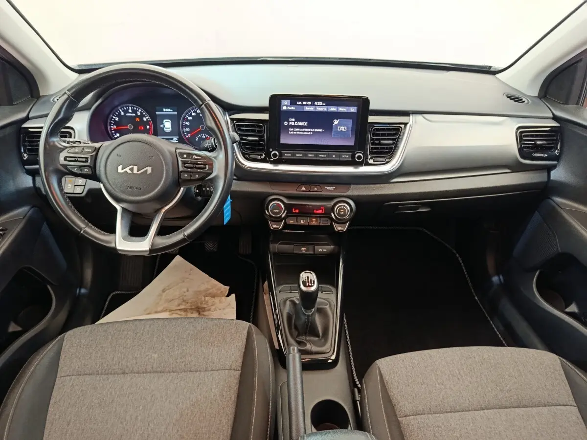 Vue intérieure frontale du tableau de bord gris et noir de la KIA Stonic 2023 avec volant cuir et écran tactile central.