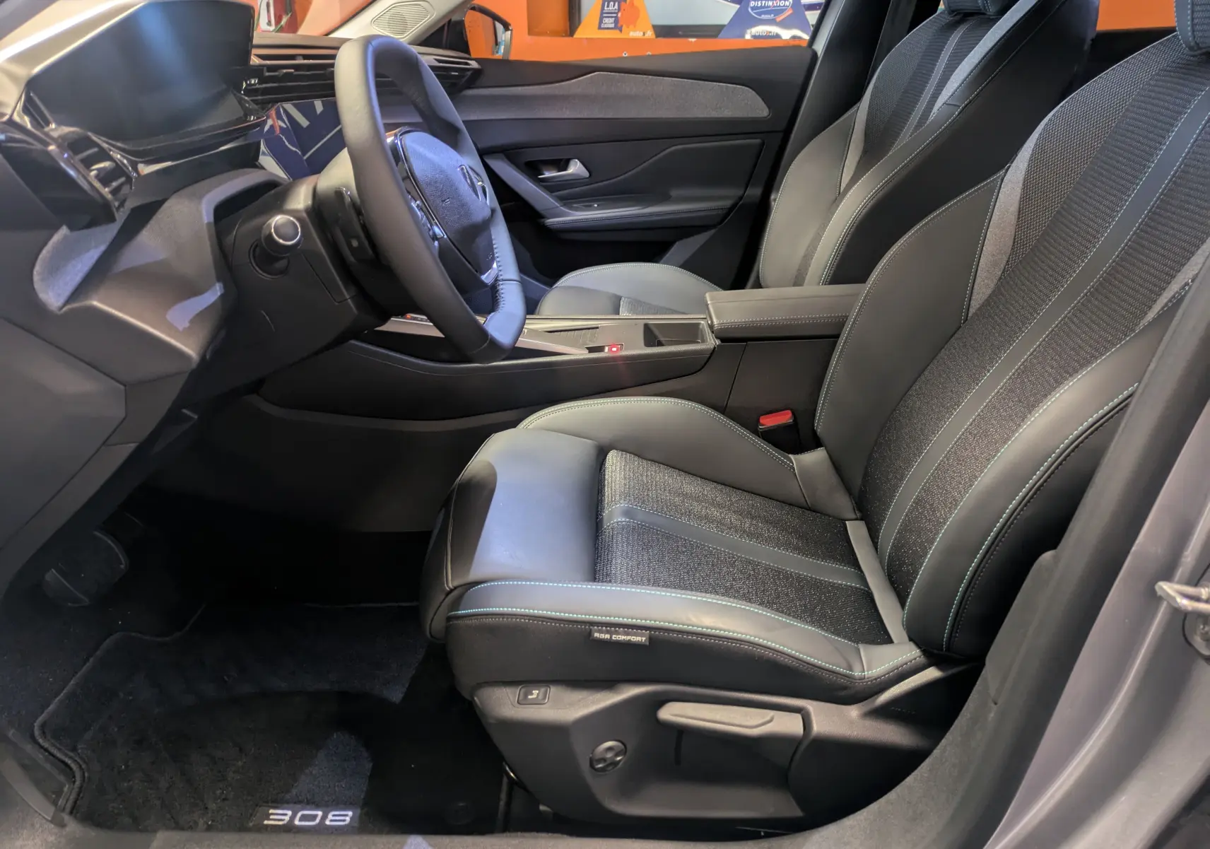 Intérieur avant droit de la Peugeot 308 2025 avec sièges en cuir et tissu gris, volant multifonction et console centrale épurée.