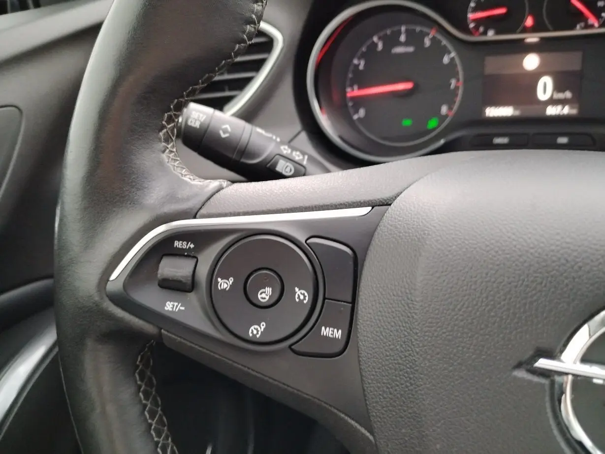 Gros plan sur le volant cuir noir de l'Opel Grandland X gris platinium, avec commandes de régulateur et tableau de bord partiel.