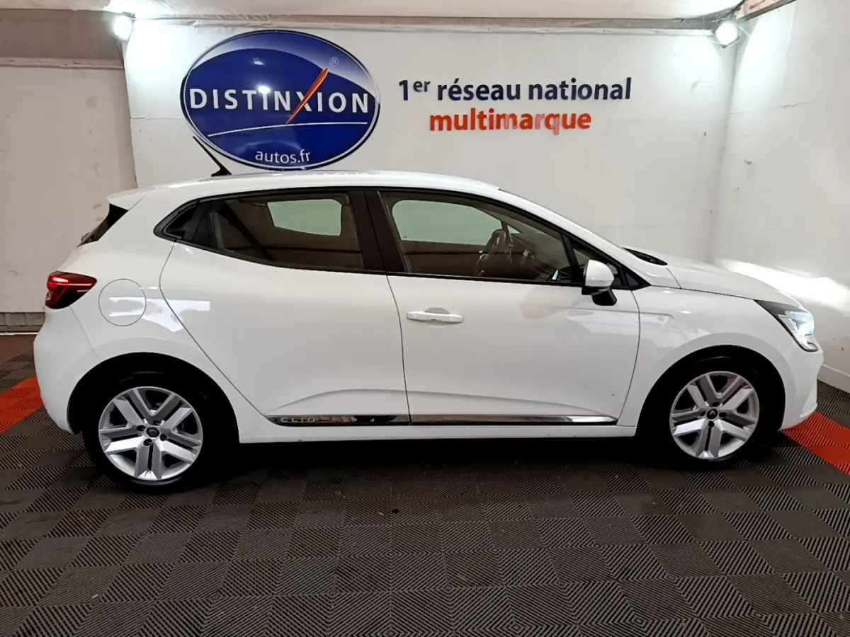 Profil côté gauche d'une Renault Clio Business Blue dCi 85 blanche, vue en intérieur avec jantes alliage et rétroviseurs blancs.