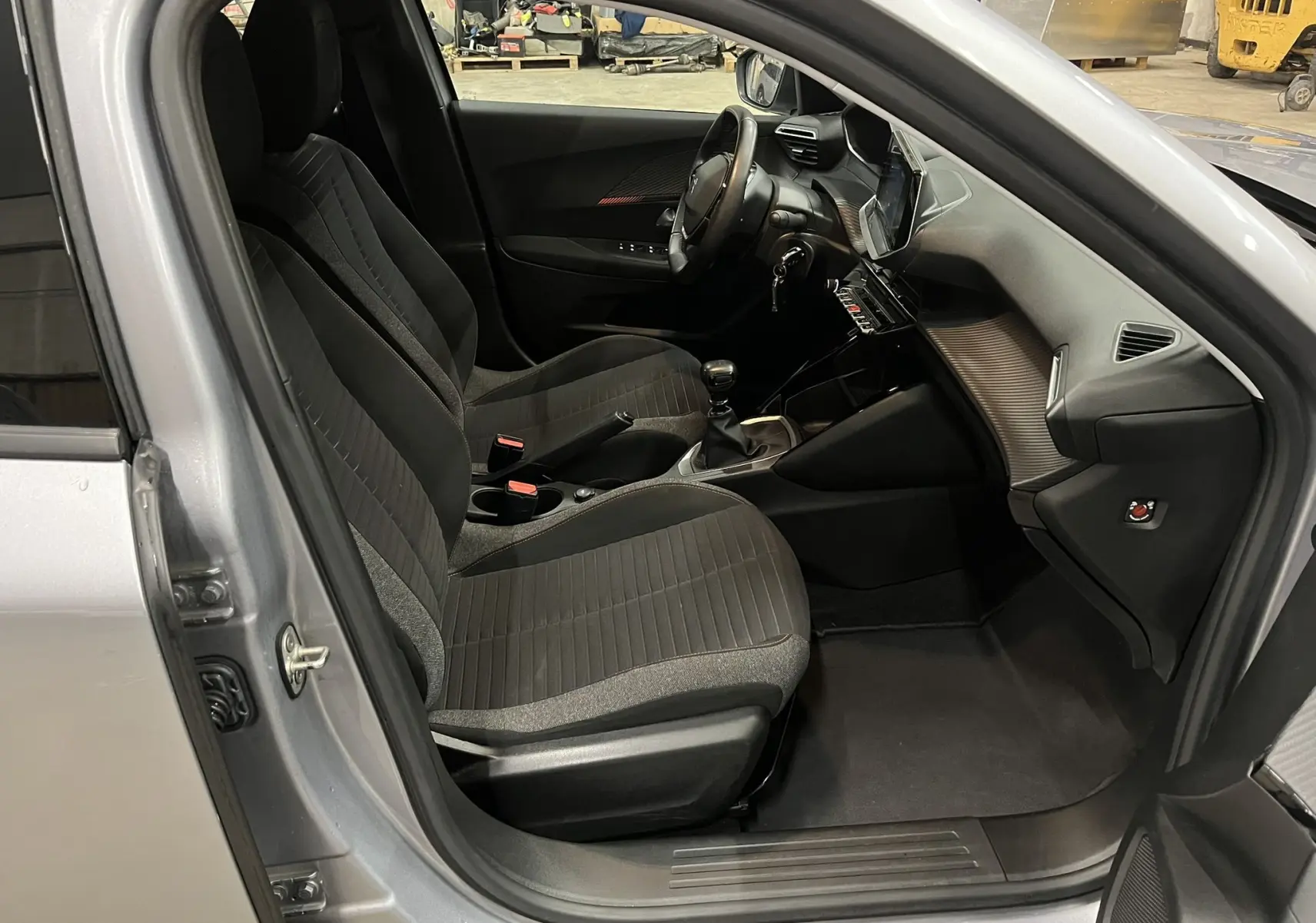 Vue intérieure côté conducteur du Peugeot 2008 gris alu, montrant les sièges noirs et la console centrale avec boîte manuelle.