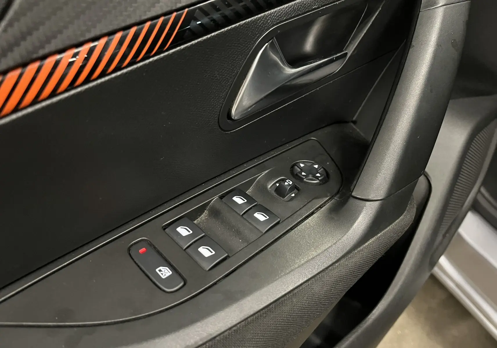 Vue rapprochée de la porte avant gauche d'une Peugeot 2008 gris alu, montrant les commandes électriques des vitres et le bouton de verrouillage.