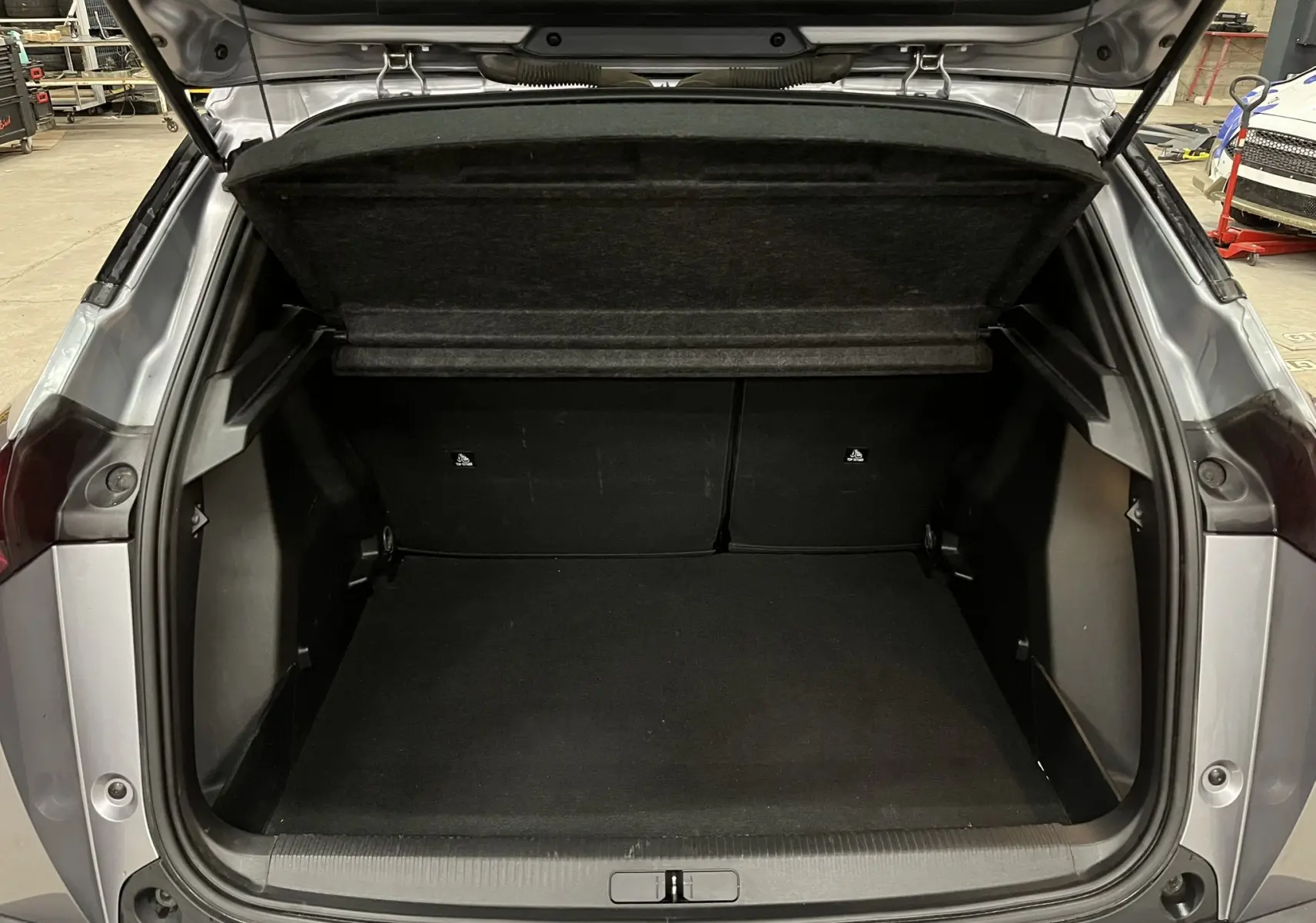 Coffre ouvert vu de l'arrière d'un Peugeot 2008 gris alu, montrant l'espace de chargement vide et la tablette arrière relevée.