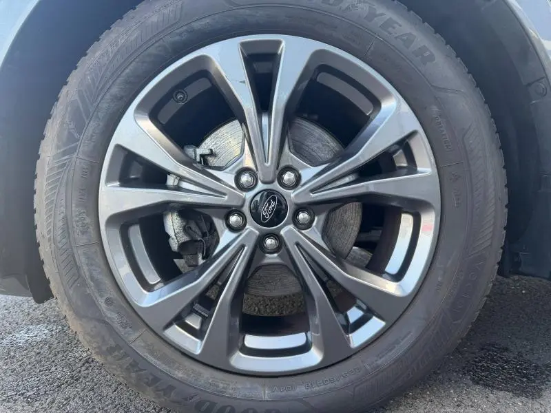 Gros plan sur la jante alu gris foncé du Ford Kuga 2024, mettant en valeur le logo central et le disque de frein visible.
