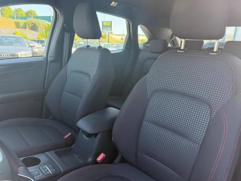Vue intérieure côté gauche du Ford Kuga 2024, sièges sport noirs avec surpiqûres rouges et accoudoir central.