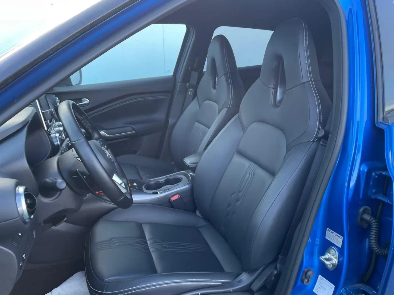 Vue intérieure côté conducteur du Nissan Juke 2024 bleu magnetic, sièges avant en TEP noir avec surpiqûres blanches.