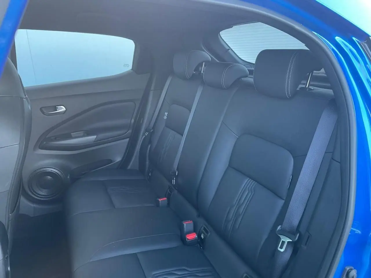 Vue intérieure sur la banquette arrière noire du Nissan Juke II 2024, avec portières et ceintures visibles en bleu magnetic.