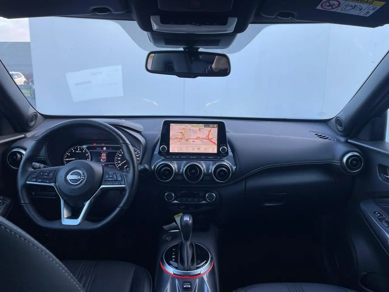 Vue intérieure avant du Nissan Juke 2024 avec tableau de bord noir, écran tactile central et volant cuir.