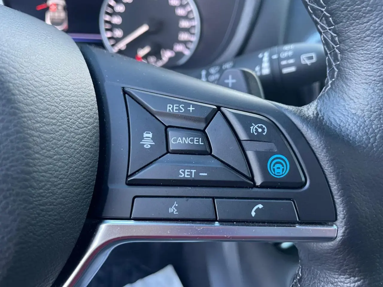 Gros plan sur les commandes de régulateur adaptatif au volant cuir du Nissan Juke II bleu Magnetic 2024