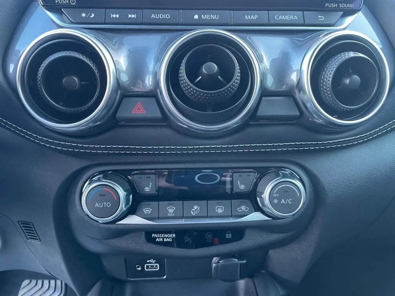 Tableau de bord noir avec commandes de climatisation et aérateurs ronds chromés du Nissan Juke II 2024 bleu magnetic