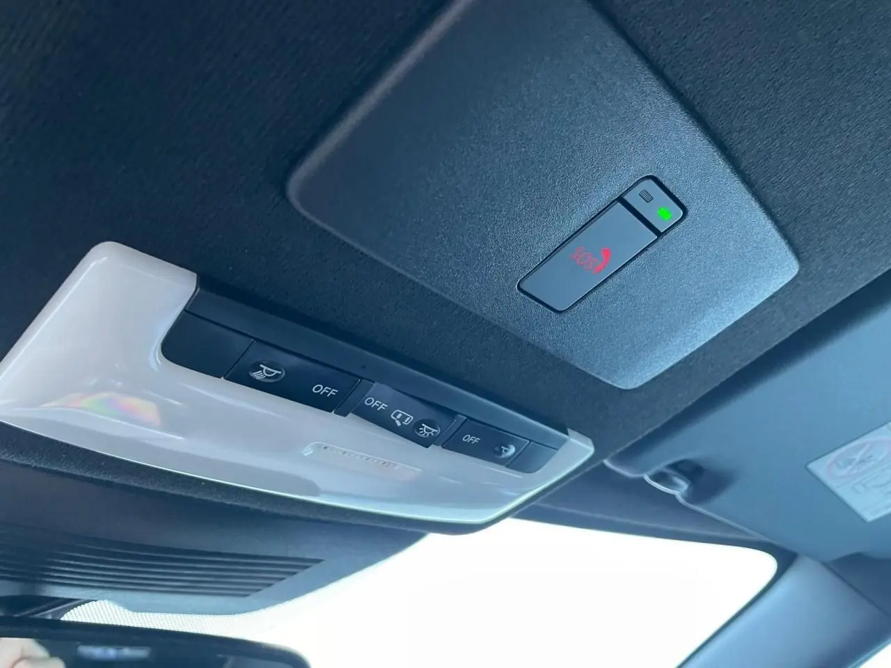 Gros plan sur la console de toit noire avec bouton SOS rouge et éclairage intérieur blanc du Nissan Juke II bleu magnetic 2024.