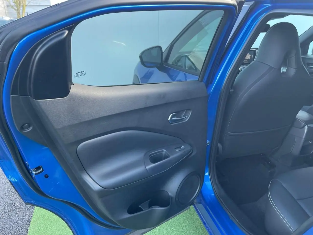 Vue intérieure côté gauche de la porte arrière ouverte d'un Nissan Juke II bleu magnetic, avec siège noir visible.