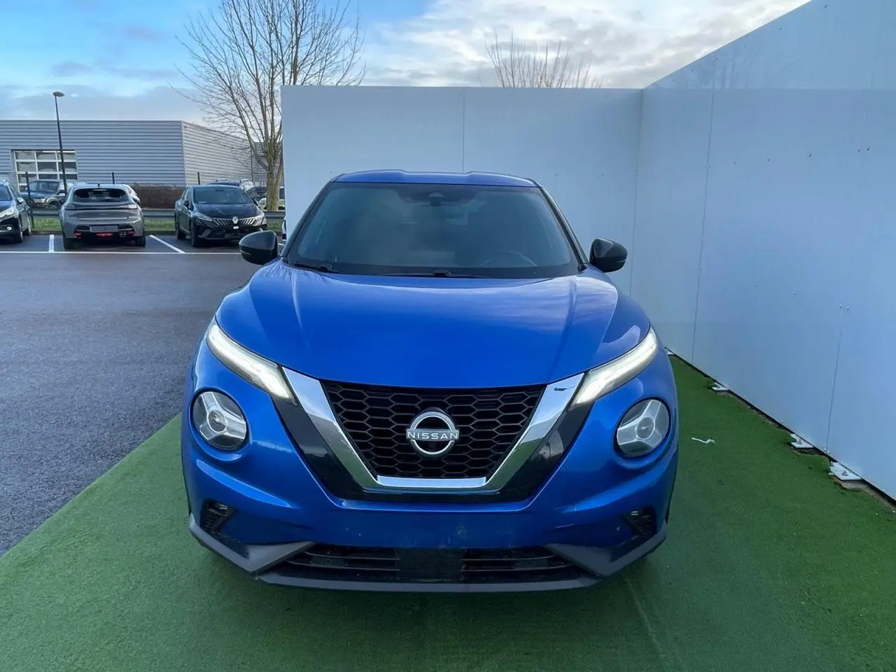 Vue avant d'un Nissan Juke II 2024 bleu magnetic avec calandre en V chromée et phares LED fins.