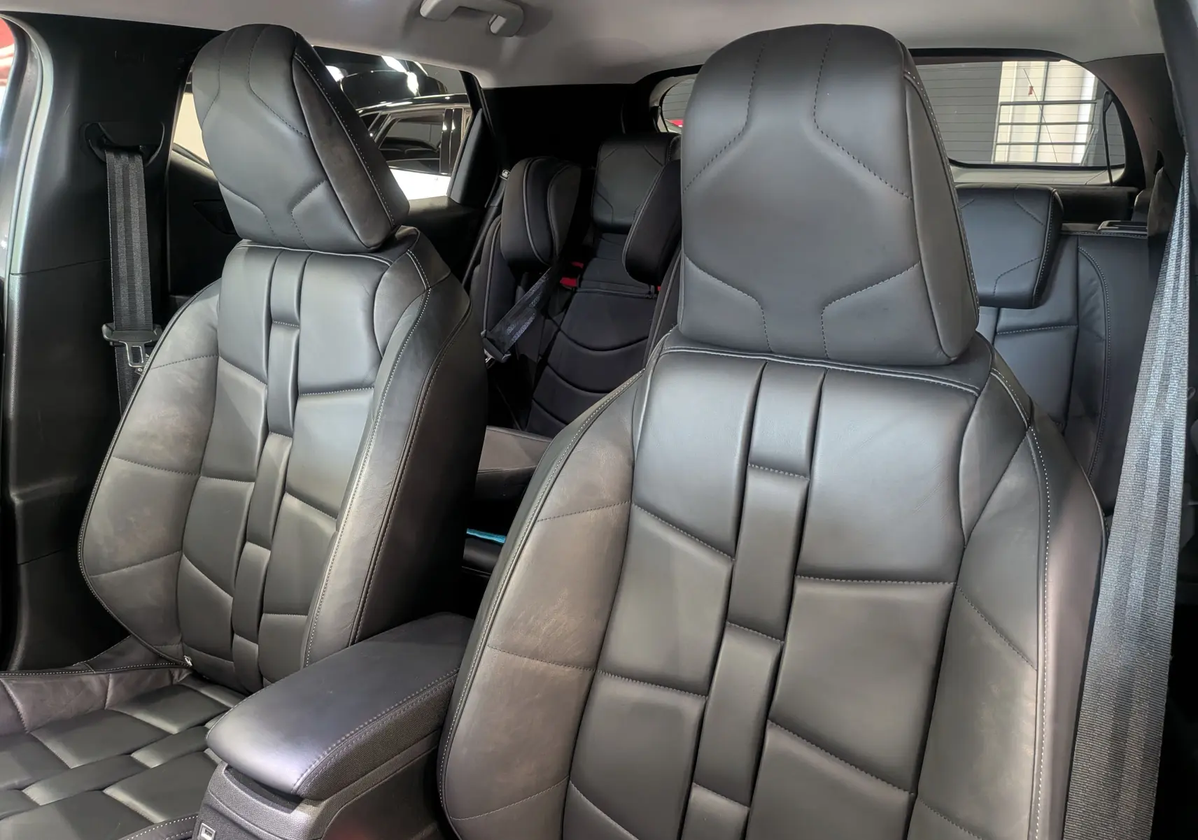 Vue intérieure rapprochée des sièges avant en cuir noir du DS3 2024, soulignant leur design géométrique et l'accoudoir central.