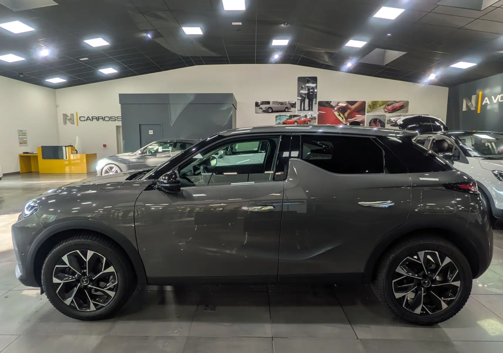 Vue de profil côté gauche d'une DS3 2024 gris Platinium avec jantes bi-ton noires dans un showroom.