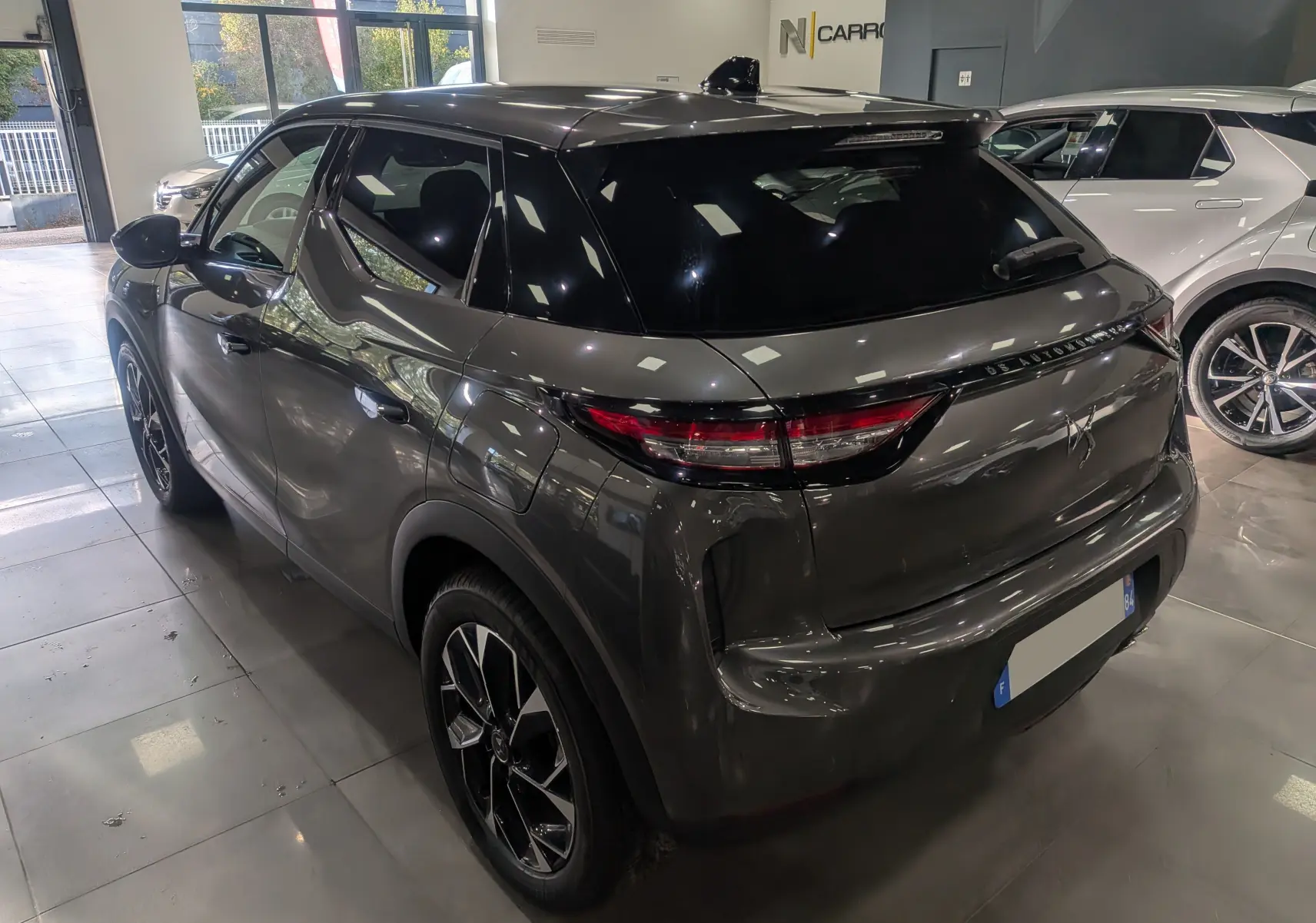 Vue 3/4 arrière droite d'un DS3 2024 gris Platinium avec toit noir brillant et feux arrière effilés en intérieur showroom.