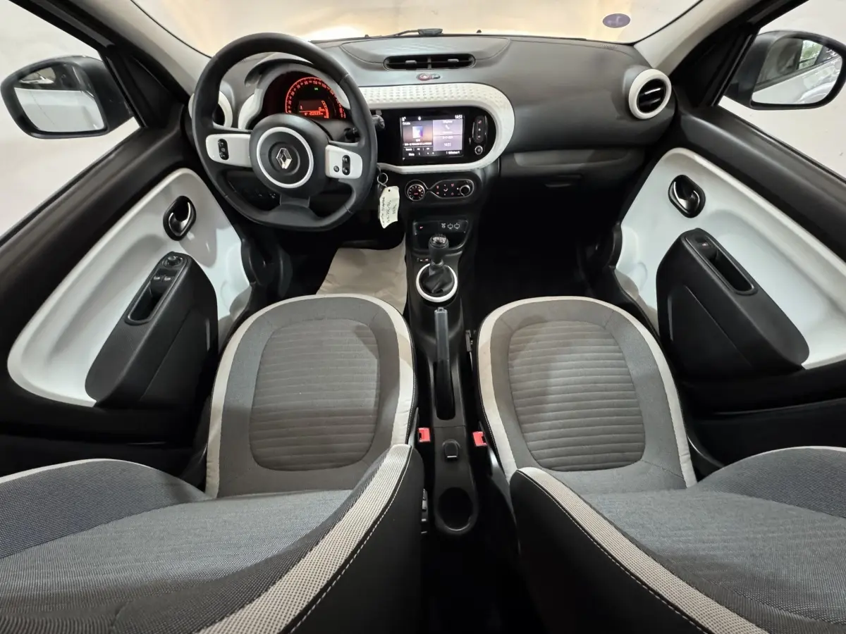 Intérieur avant de la Renault Twingo blanc et gris, vue centrée sur le tableau de bord et les sièges avant.