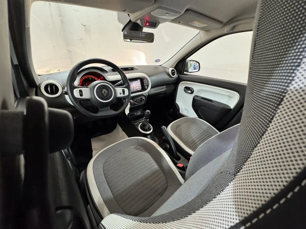 Intérieur Renault Twingo blanc vu côté conducteur, volant multifonctions, tableau de bord avec écran tactile et sièges gris.