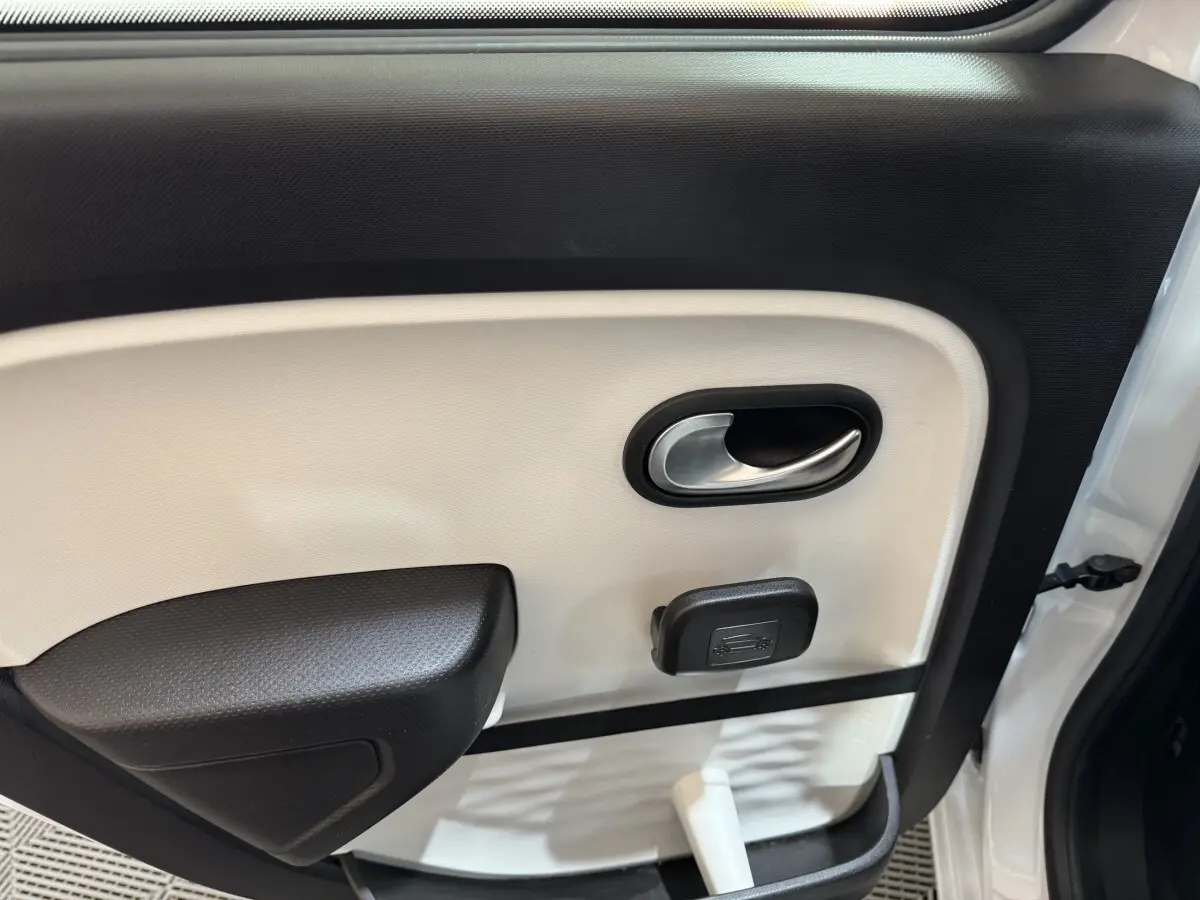 Gros plan sur la porte intérieure côté gauche de la Renault Twingo blanche, montrant la poignée et le bouton d'ouverture du coffre.