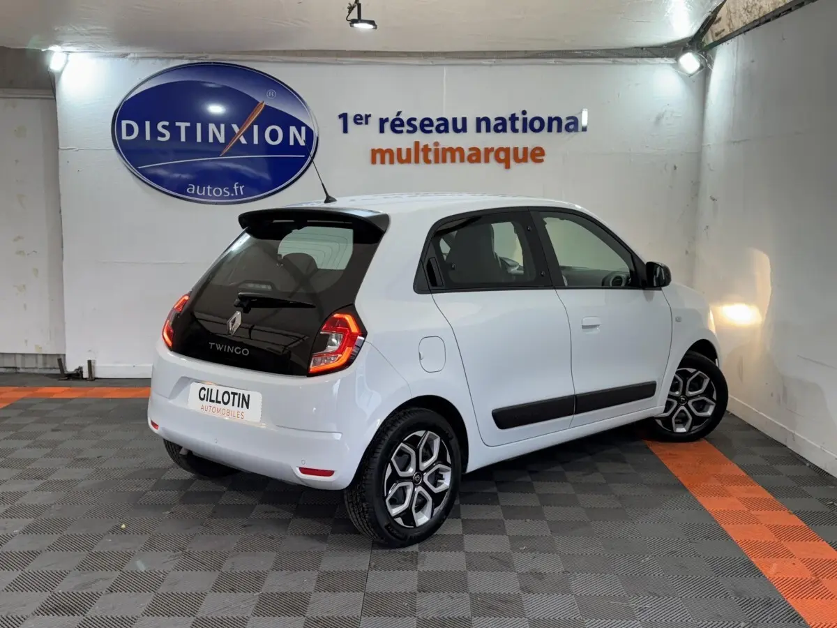 Renault Twingo Equilibre blanc vue 3/4 arrière droit en intérieur avec jantes distinctives et vitres teintées.