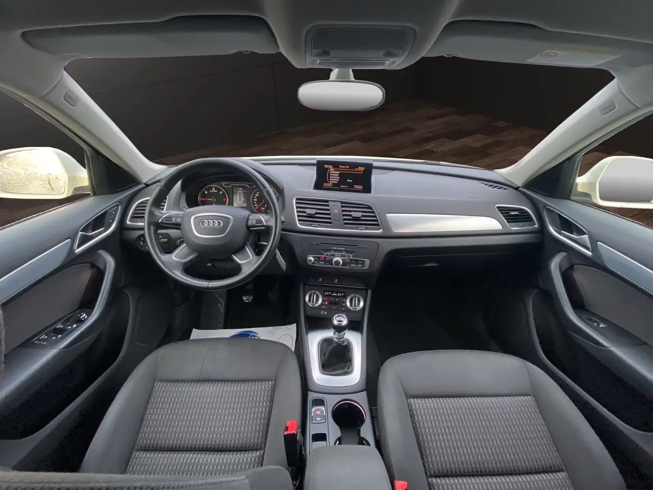 Vue intérieure avant de l'Audi Q3 2.0 TDI 2014 avec tableau de bord noir, volant cuir et écran GPS central.