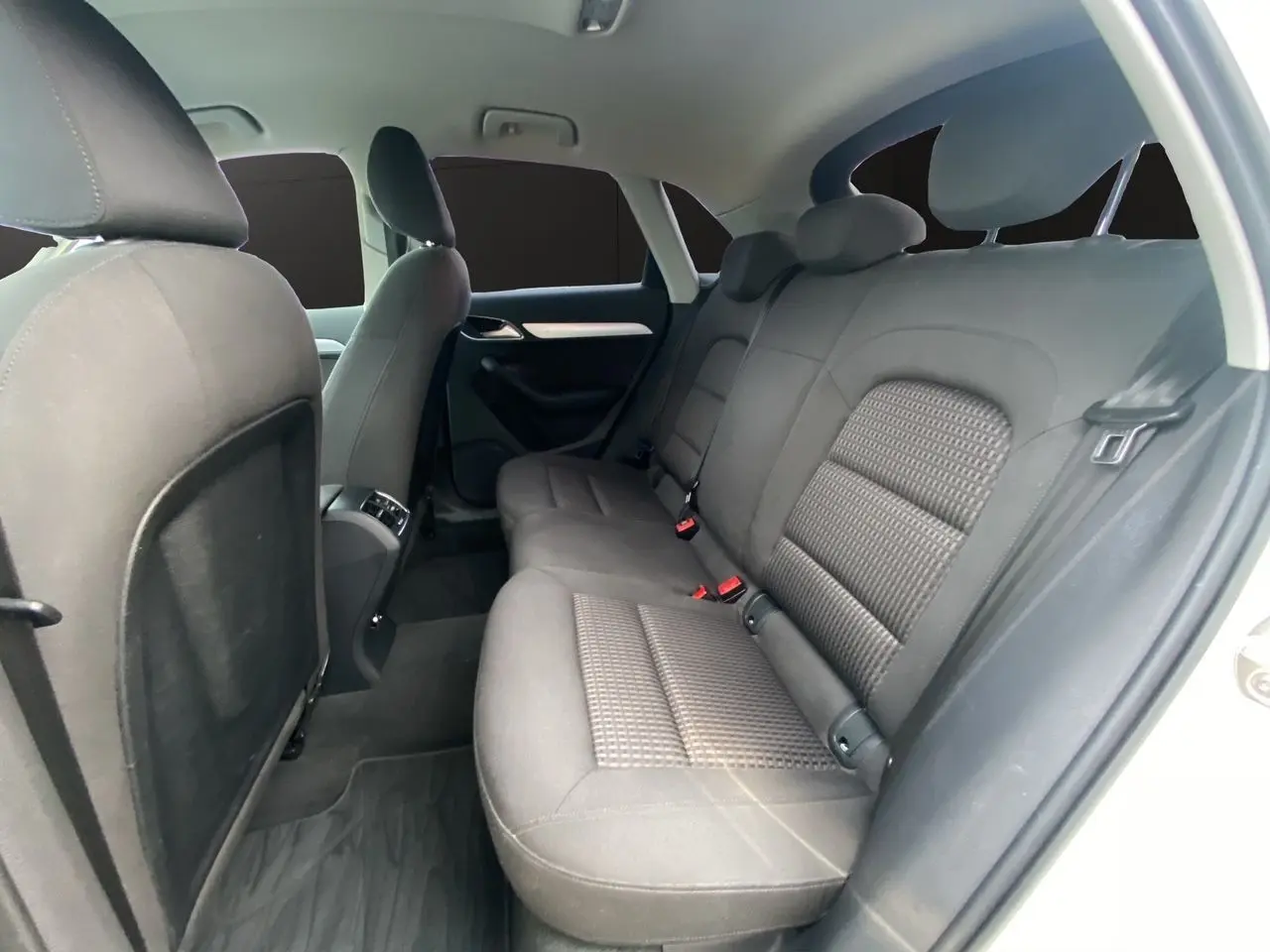Vue intérieure montrant les sièges arrière en tissu noir de l'Audi Q3 blanc, version 2014, avec portes ouvertes côté droit.