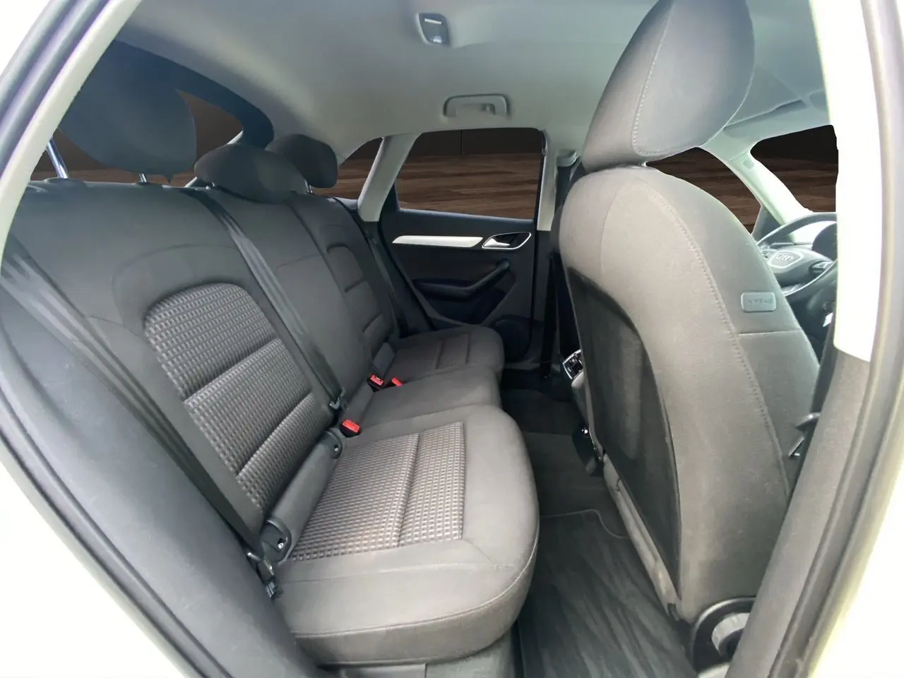 Vue intérieure arrière droite de l’Audi Q3 blanc 2014, sièges tissu noir avec vitres arrière surteintées.