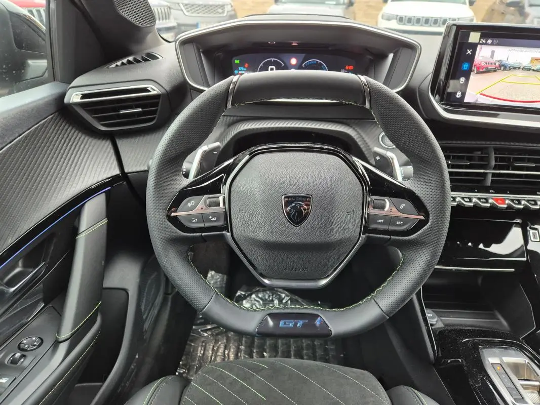 Vue intérieure centrée sur le volant GT de la Peugeot 208 gris, avec cockpit numérique et écran tactile visible.