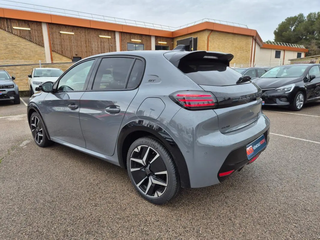 Peugeot 208 Hybrid 110 GT gris vue 3/4 arrière droit, jantes alliage 17 pouces et feux arrière LED allumés.