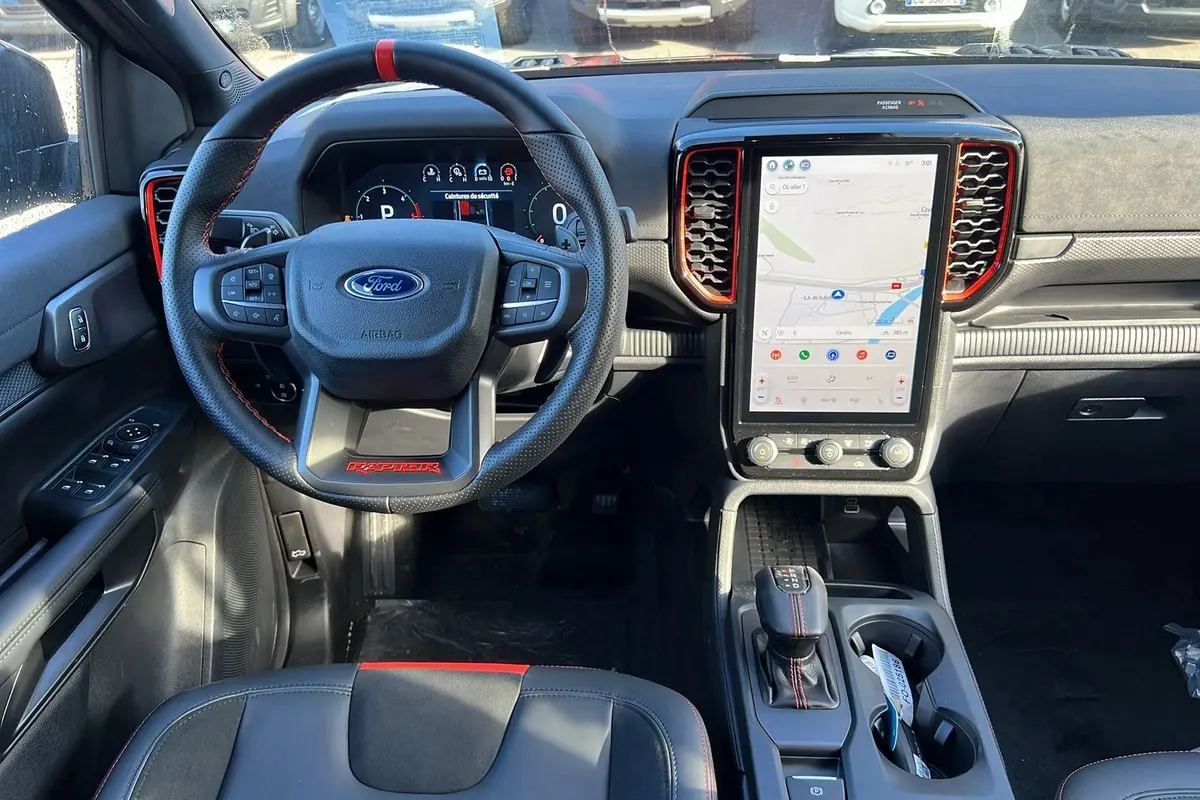 Vue intérieure avant du Ford Ranger Raptor noir, volant cuir avec surpiqûres rouges et grand écran tactile vertical central.