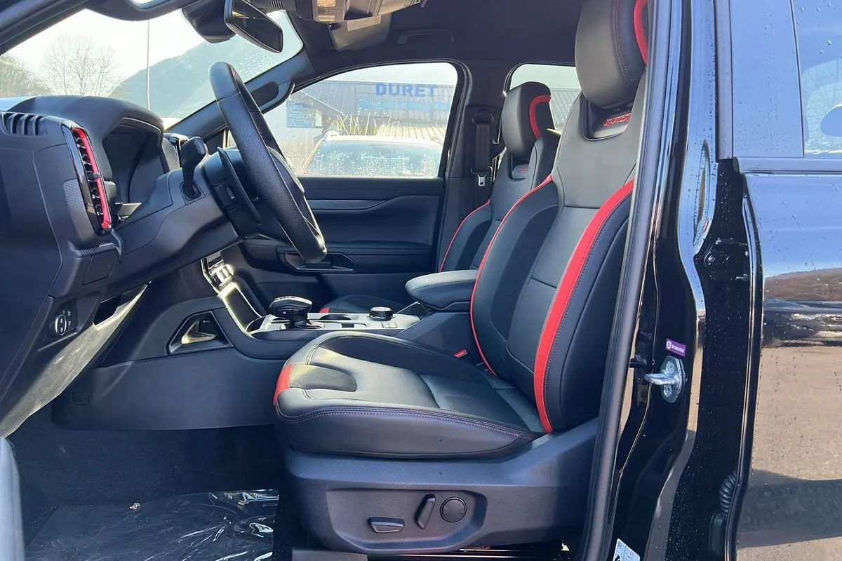 Vue intérieure côté conducteur du Ford Ranger Raptor noir absolu 2025, sièges sport noirs avec surpiqûres rouges et volant cuir multifonctions.