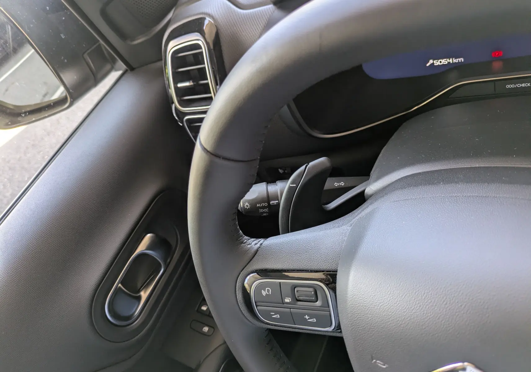 Vue rapprochée du volant noir en croûte de cuir côté gauche du Citroën C5 Aircross Hybride 2025 avec commandes intégrées.