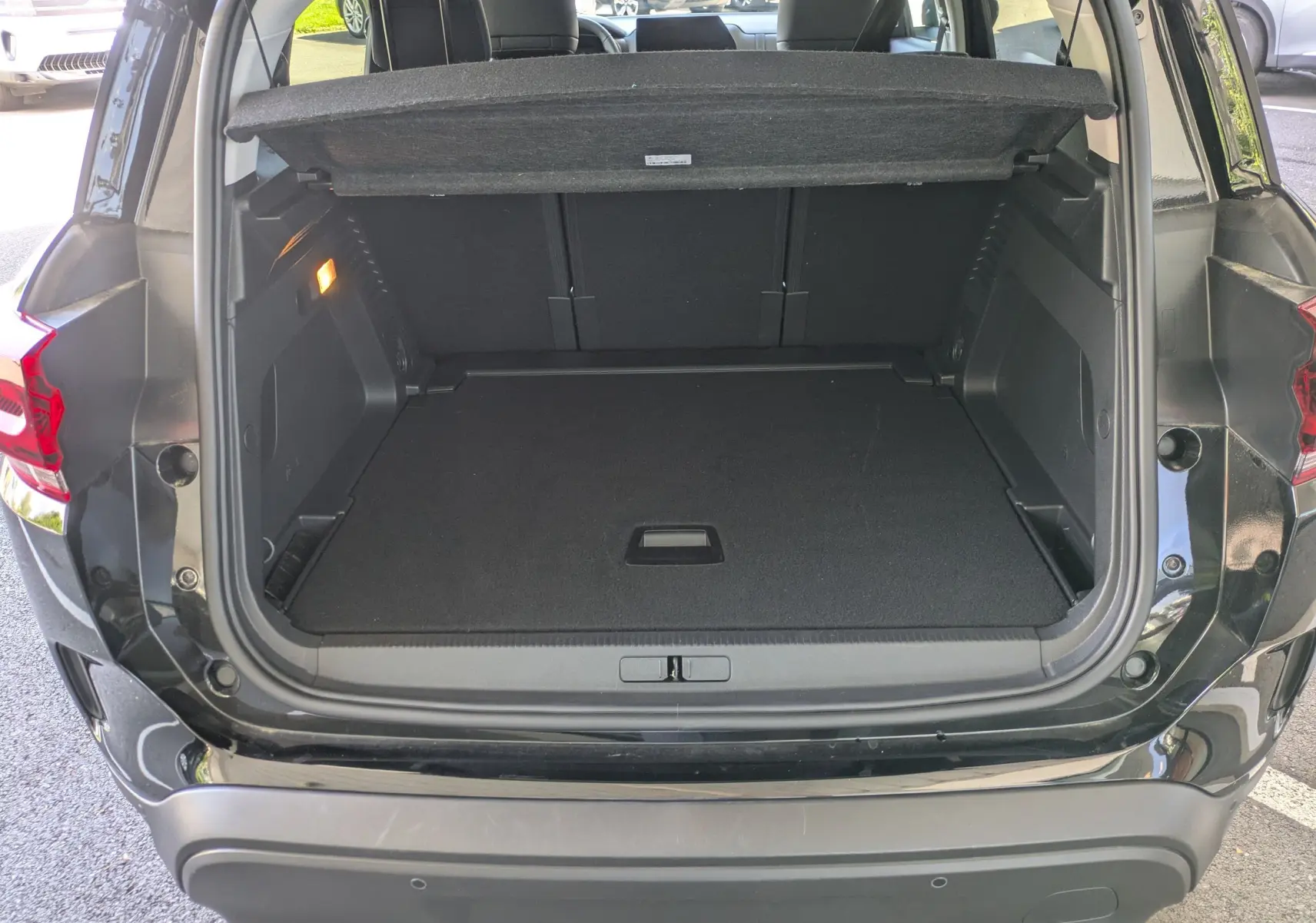 Coffre ouvert vu de l'arrière d'un Citroën C5 Aircross hybride noir perla avec intérieur de coffre spacieux et tapis noir.