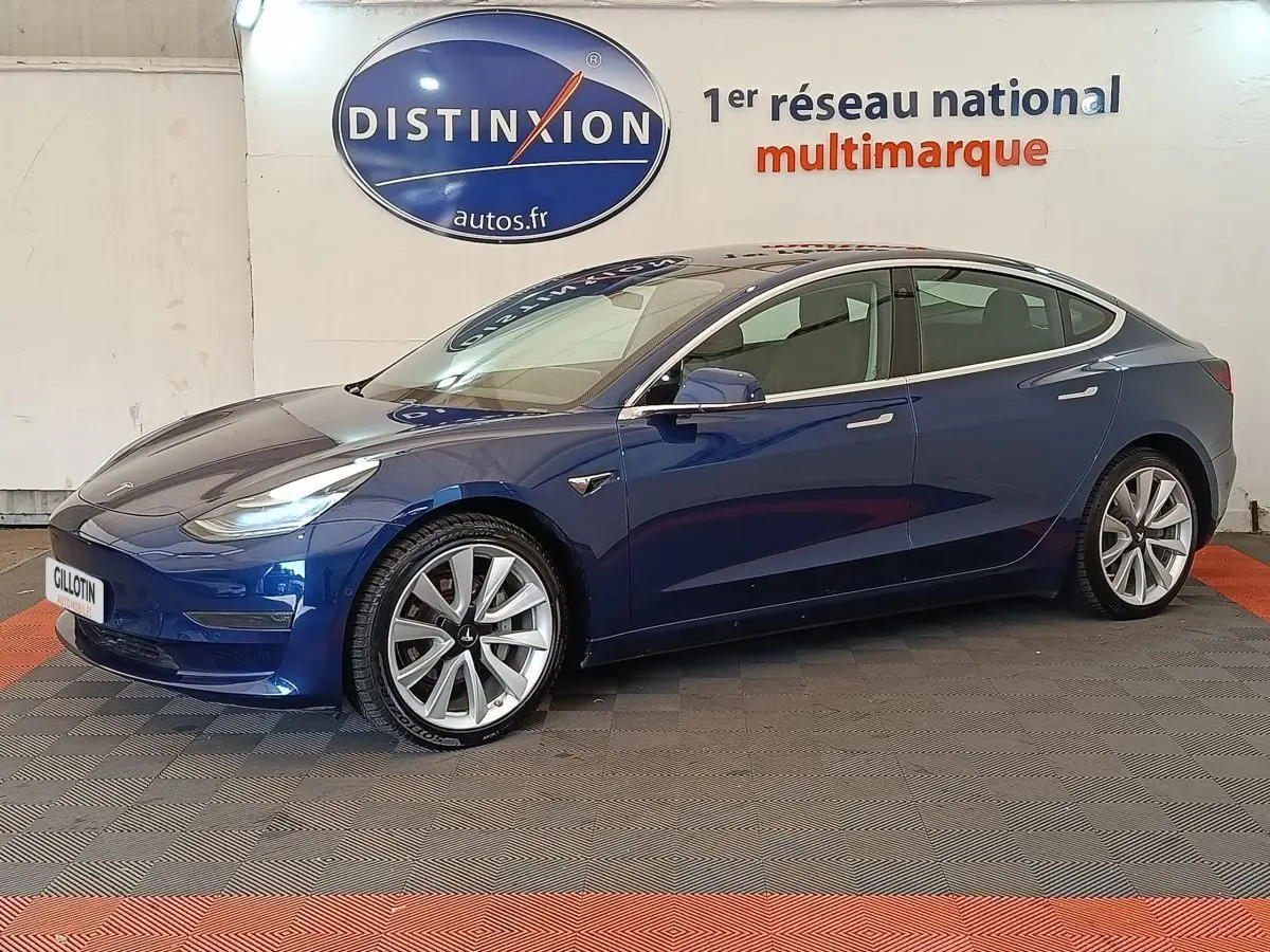 Tesla Model 3 Long Range bleu en vue profil côté gauche, avec jantes alliage et rétroviseurs électriques visibles.