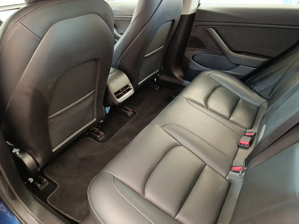 Vue intérieure côté arrière droit montrant la banquette en cuir noir et les dossiers des sièges avant d'une Tesla Model 3 bleu.