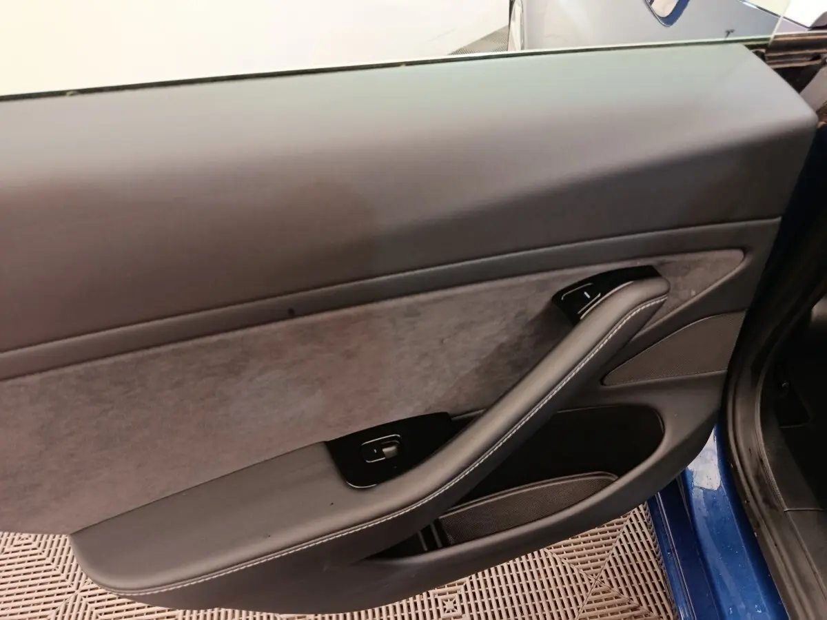Vue intérieure du panneau de porte côté gauche d'une Tesla Model 3 bleu, avec accoudoir en cuir et commande de fenêtre.