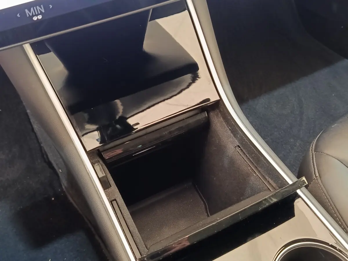 Vue rapprochée de la console centrale noire brillante avec rangement ouvert et accoudoir cuir dans une Tesla Model 3 bleu.