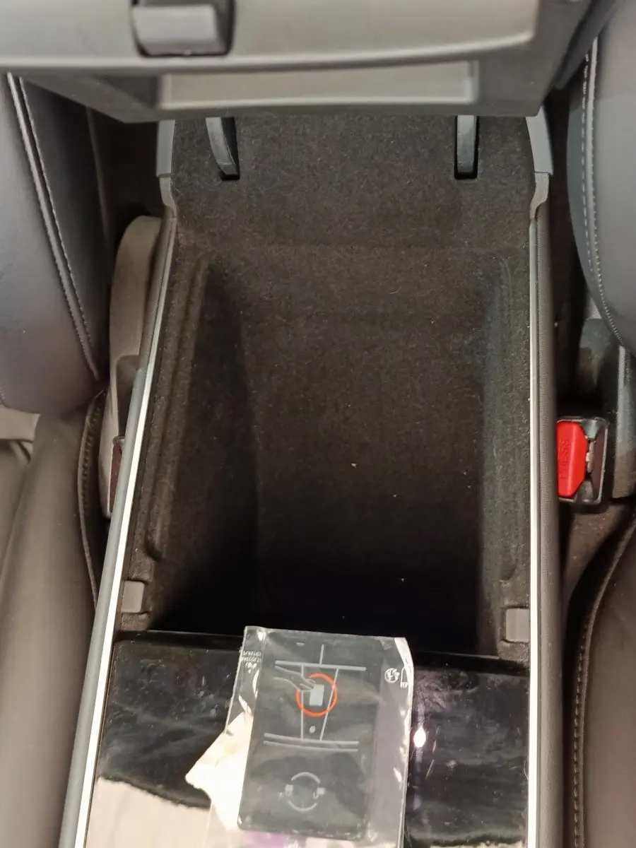 Vue rapprochée de la console centrale ouverte d'une Tesla Model 3 Long Range bleu, montrant un compartiment vide et un manuel.