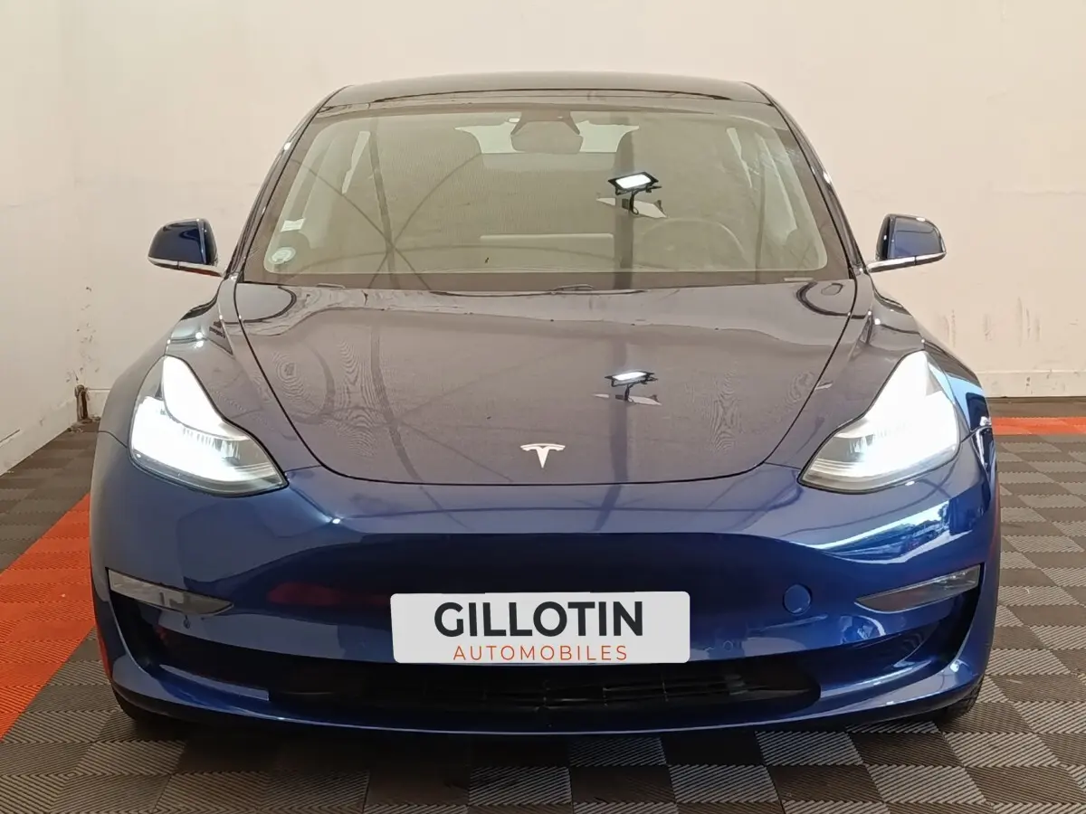 Vue frontale d'une Tesla Model 3 Long Range AWD bleu électrique avec phares allumés en intérieur.